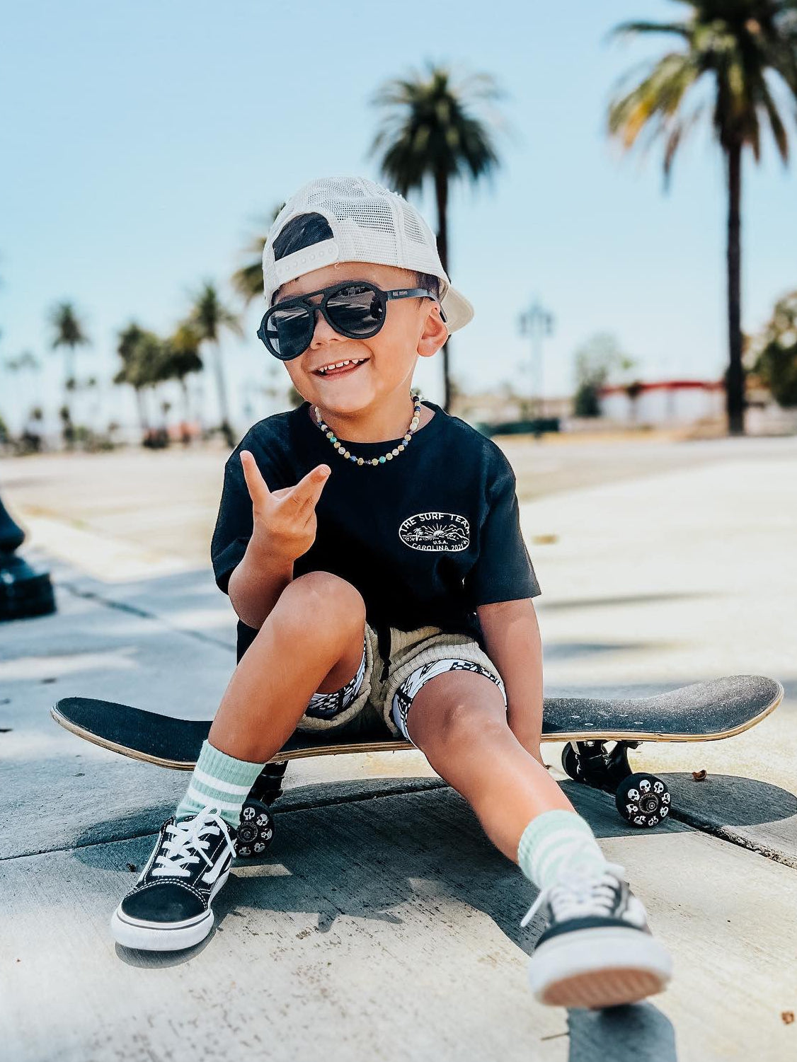 Child sitting on a skateboard in a park with palm trees in the background