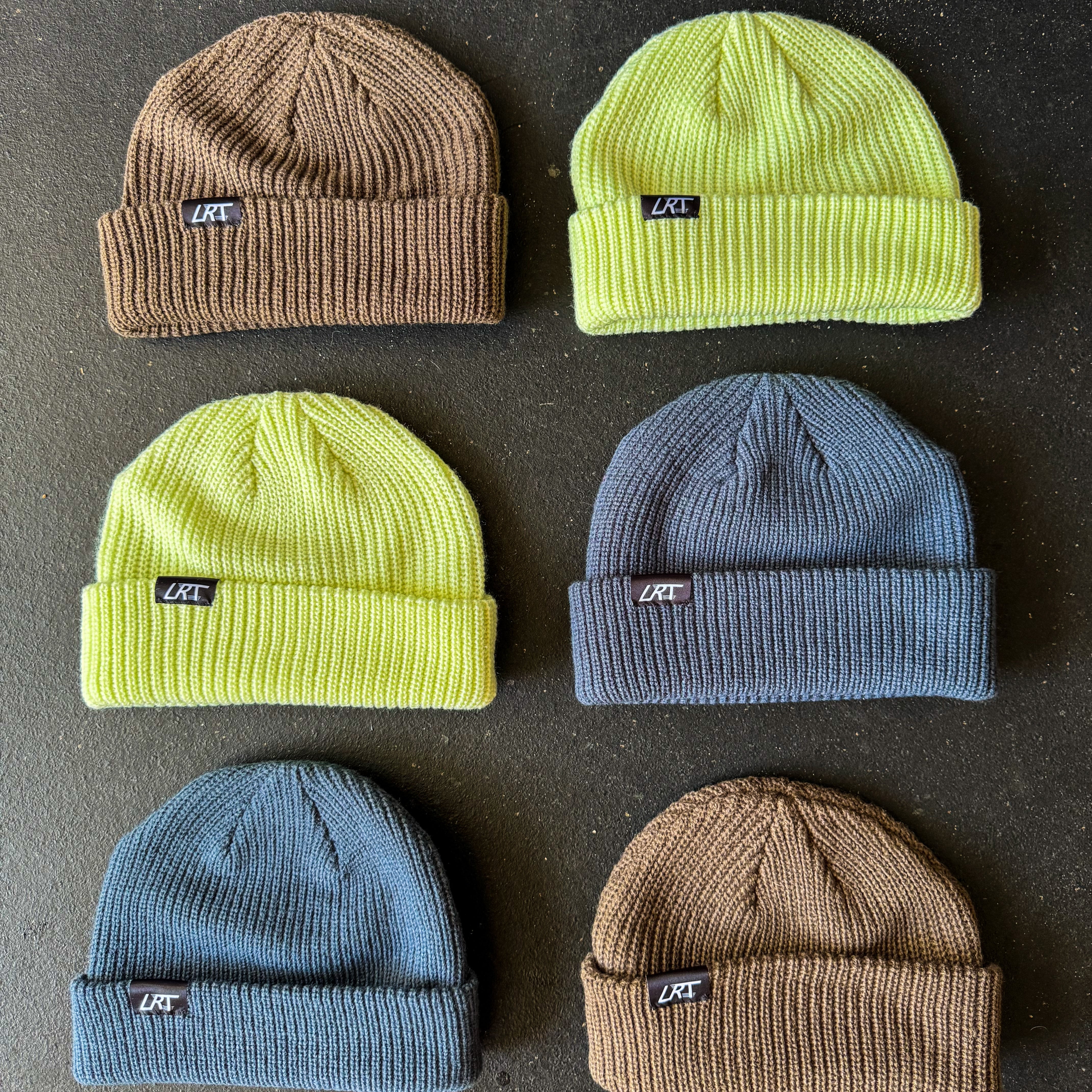 Six beanies in brown, green, and blue on a dark surface