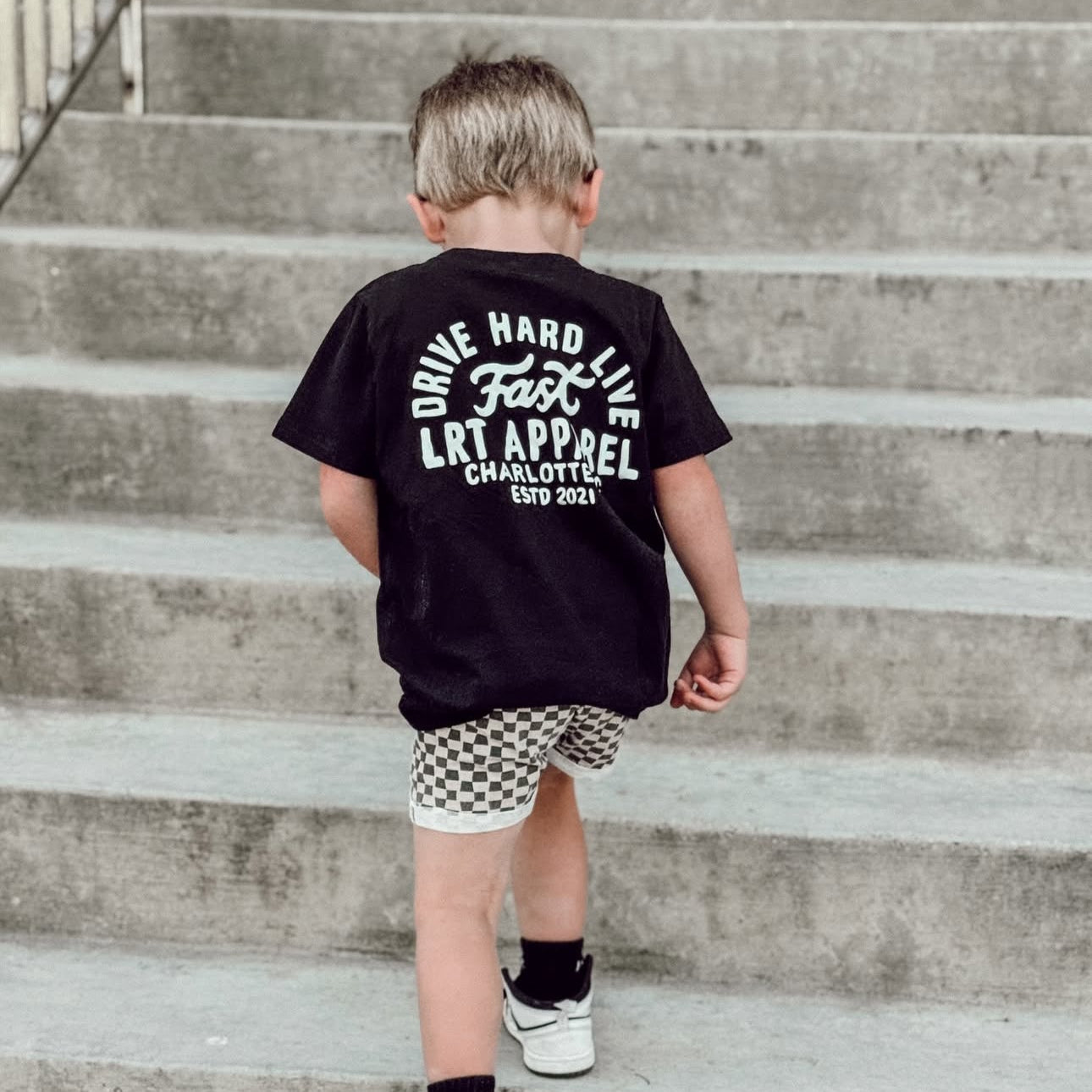 Child wearing a black t-shirt with text, walking up concrete stairs.