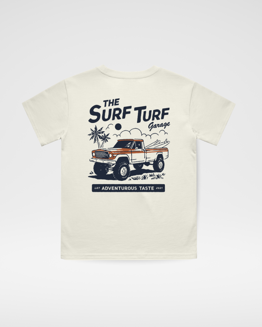 An off-white short-sleeve t-shirt with a vintage-style graphic on the front featuring a white and orange truck, palm trees, and the text 'THE SURF TURF Garage' and 'for ADVENTURERS, TASTE.