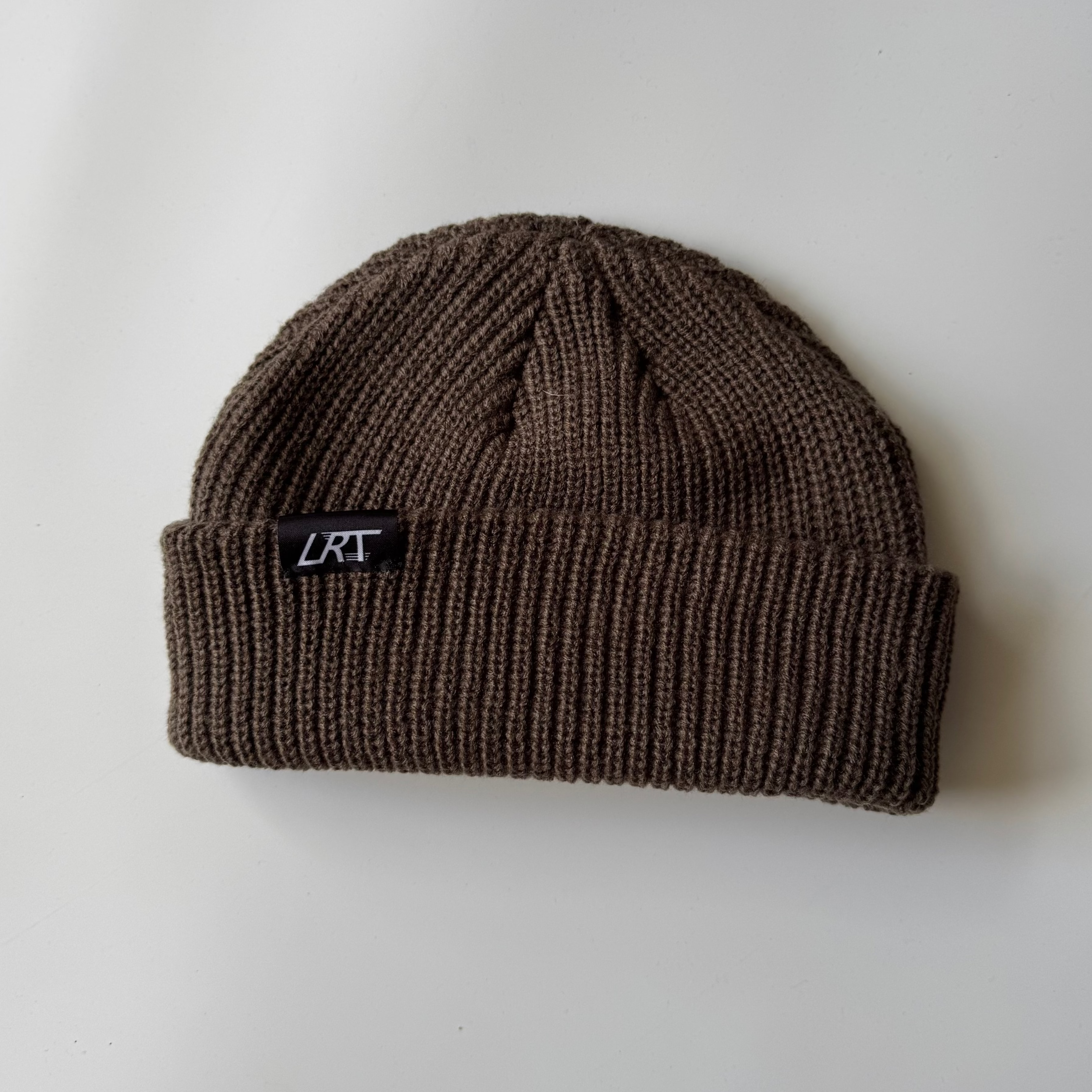 Brown knit beanie with a logo on a light gray background