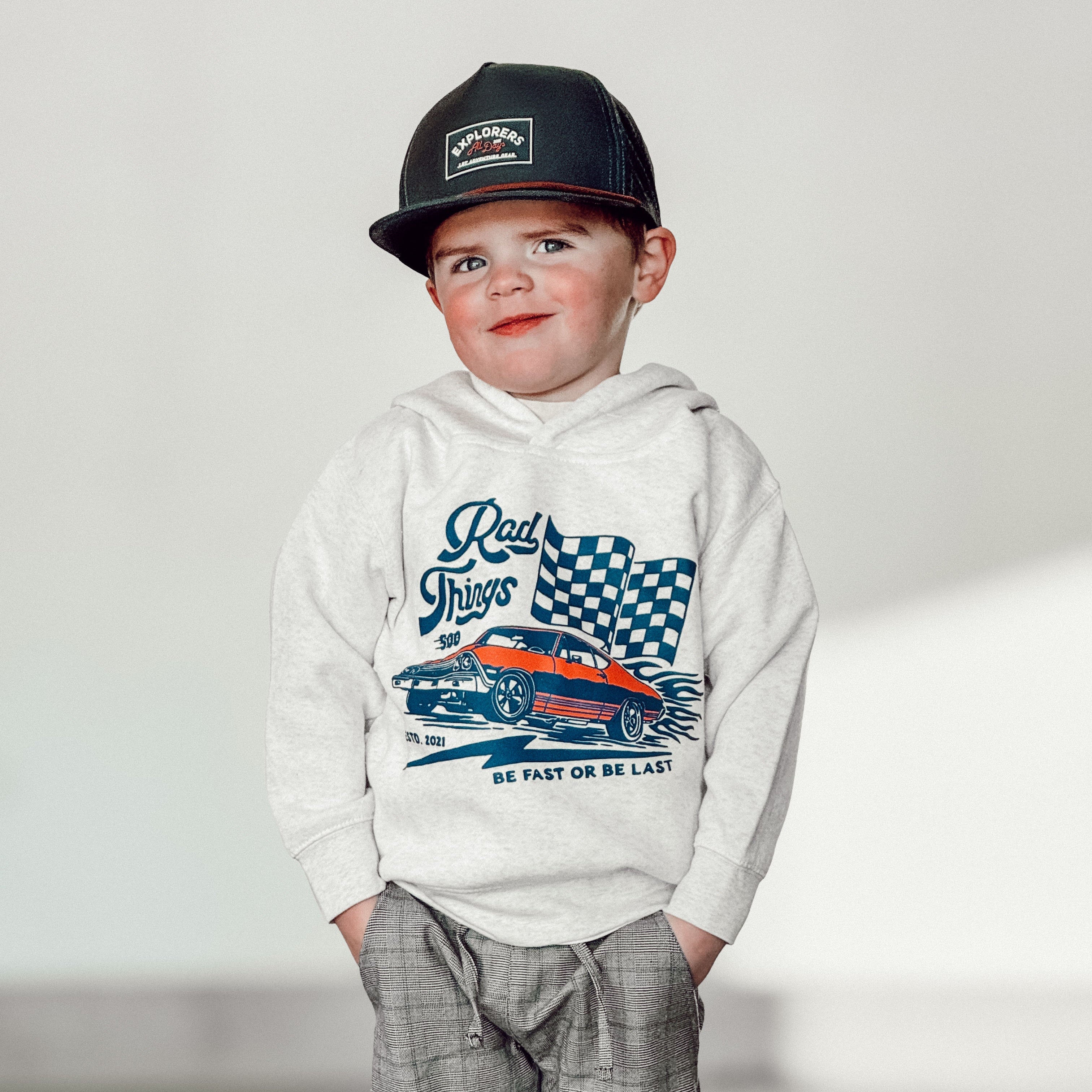 Child wearing a hoodie with a car graphic and plaid pants on a plain background