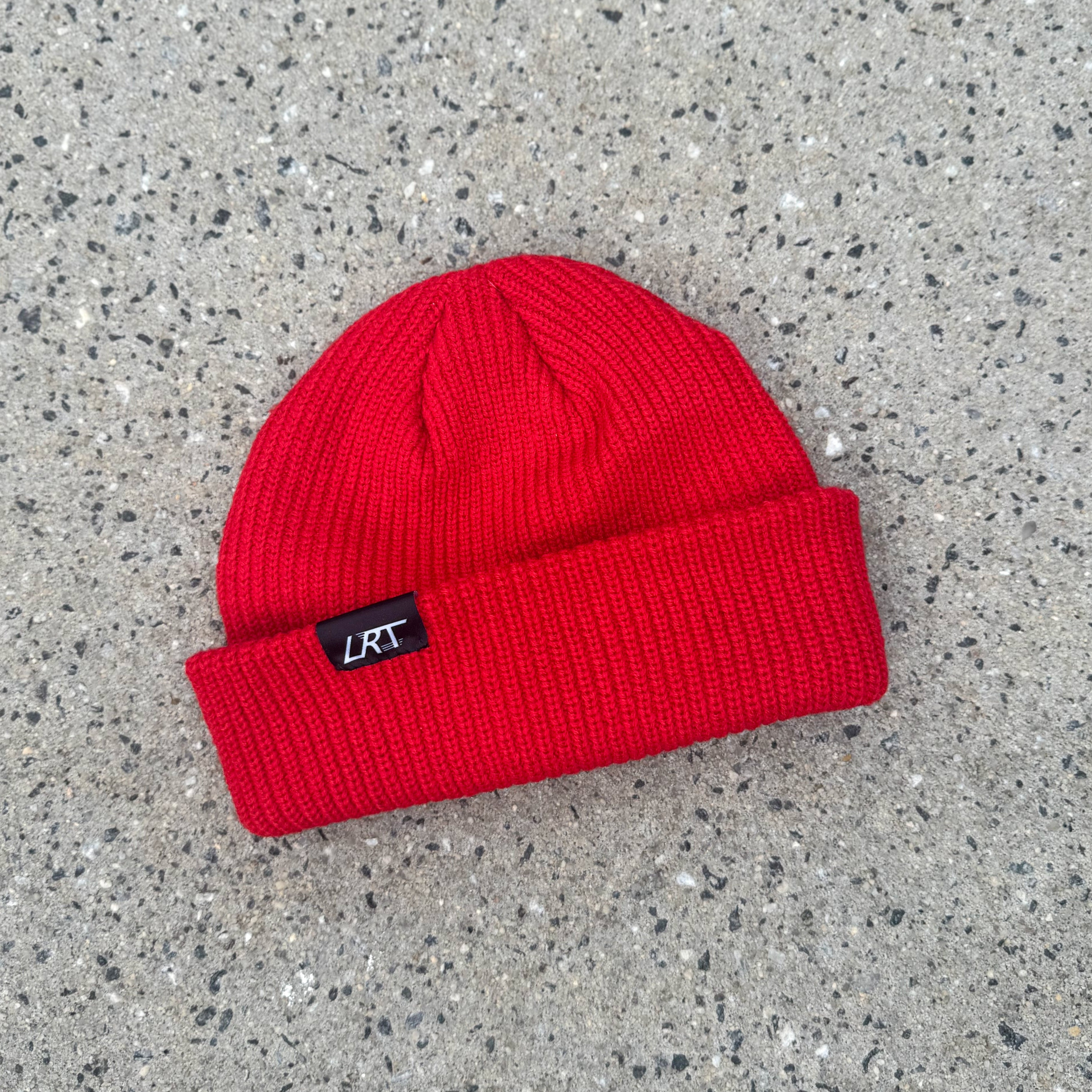Red beanie with a brand label on a gray concrete surface