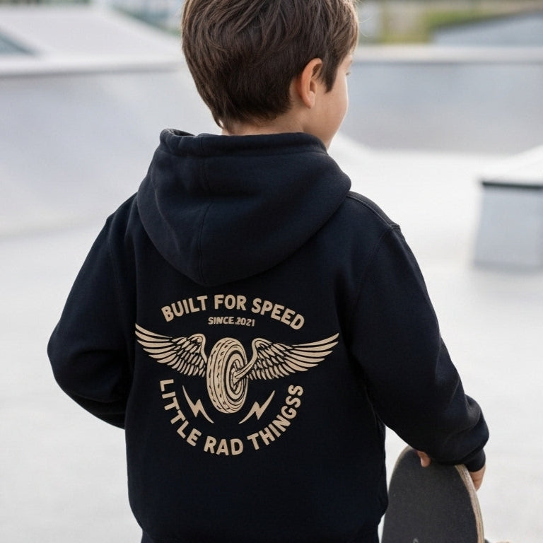Child wearing a black hoodie with text and graphics, standing at a skate park.